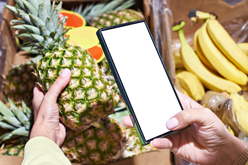 Fruit pineapple in hand and smartphone in store