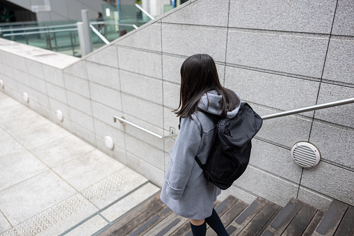 Rear view of teenage girl walking to school in city