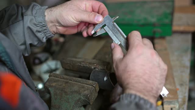 Mature Man Measuring A Piece Of Metal With A Caliper In A Workshop