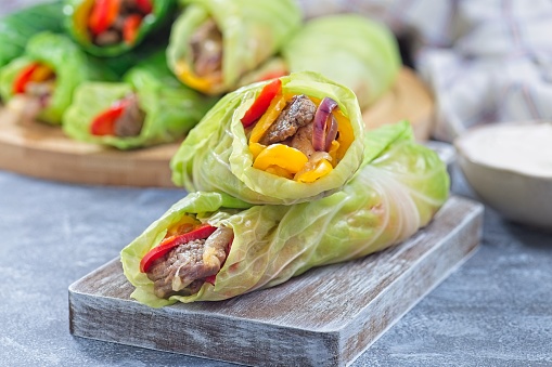 Beef and vegetable cabbage leaves wraps, served with plain yogurt, on a wooden board, horizontal