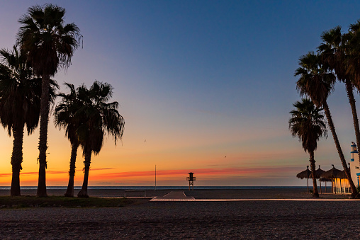 Sunrise on Poniente beach, Motril, Granada, with palm trees, a beach bar and a watchtower for bathers.