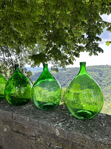 A line of big round green vintage bottles placed neatly on top of a stone wall, creating a decorative display.