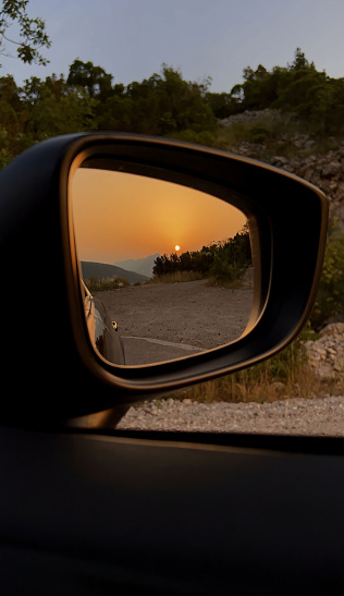 A rear view mirror on a car reflecting a stunning sunset in the background.