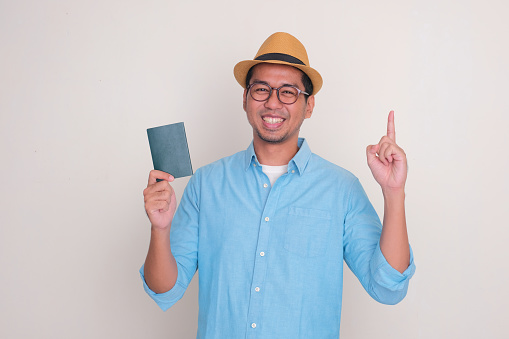 A man wearing beach hat smiling and pointing up while holding passport document