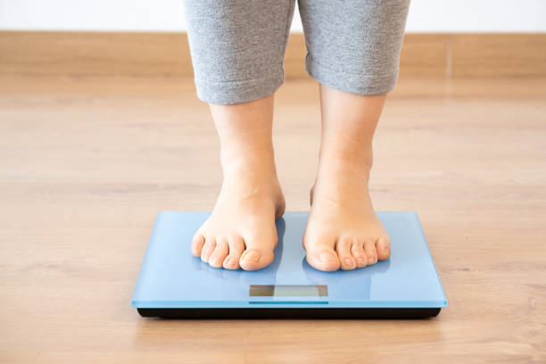 istock woman weighing herself on a scale at home 2149507808