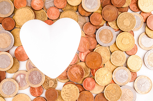 A pile of coins and a white heart. The heart is surrounded by coins of different sizes and colors. Concept of abundance and generosity, as the heart represents love and the coins symbolize wealth