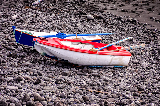 A small red and white boat is sitting on a rocky beach. The boat is upside down and he is in a state of disrepair. Concept of abandonment and neglect
