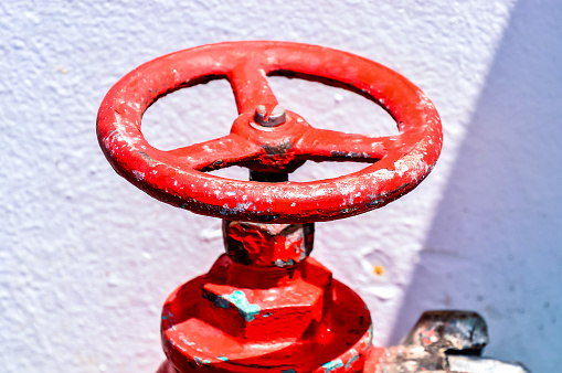 A red valve with a white background. The valve is old and rusty