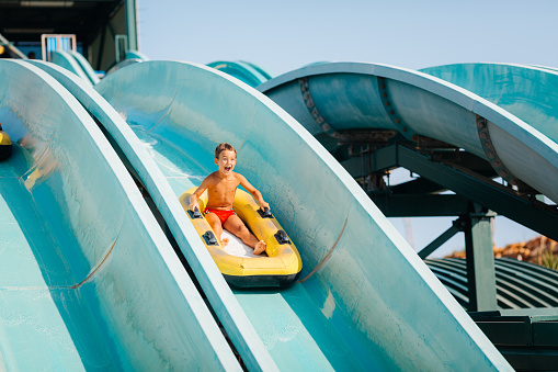 Cheerful boy having fun in waterpark sitting on a inflatable ring and sledging on the tobogan