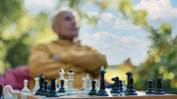 istock Blurred senior man contemplating next move in chess game outdoors. Strategy and concentration in serene park setting 2149510518
