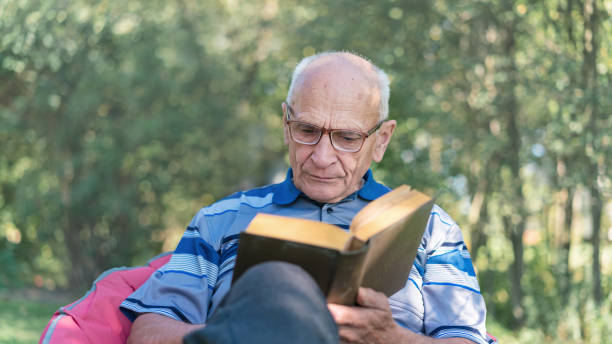 istock Engrossed elderly man reading book in peaceful outdoor setting surrounded by trees. Intellectual leisure in nature embrace enhances wellbeing and serenity 2149510520