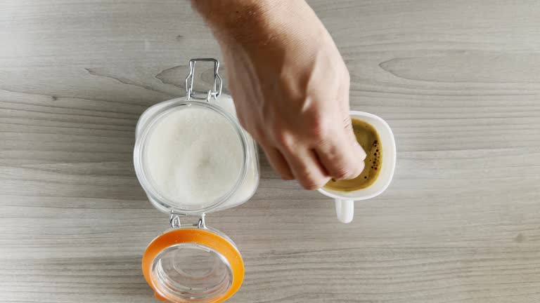 Hand adding a teaspoon of sugar to fresh brewed black coffee