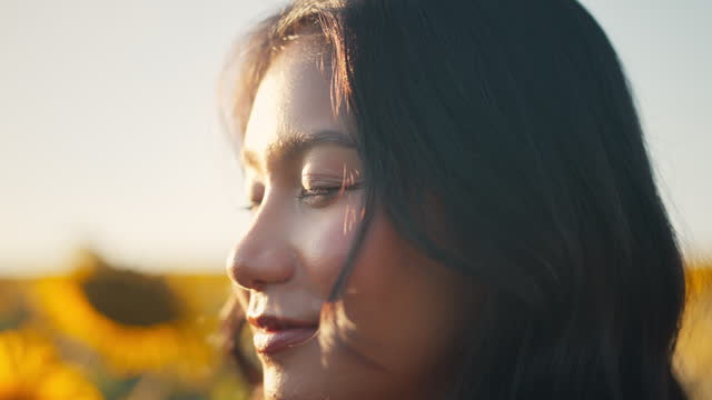 Closeup face of Asian woman opening eyes on sunset background. Young female looking straight at the sunflower field landscape.