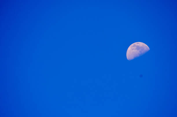 A large moon is in the sky above a blue sky. The moon is the only object in the image