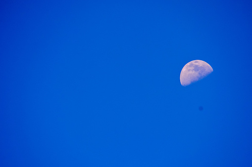 A large moon is in the sky above a blue sky. The moon is the only object in the image