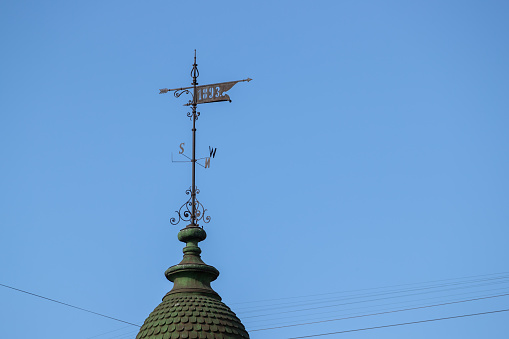 A weathervane on a slate roof against a blue sky with clouds. Room has been left for copy space.