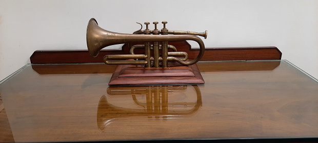 An antique bugle placed on top of a table with its reflection.\nThis was a piece used by one of the old kings of Tamilnadu, this was photographed during a visit to Otty and antique house.