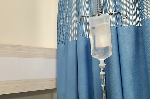 saline bag hanging in emergency room at hospital. Blue curtain as background