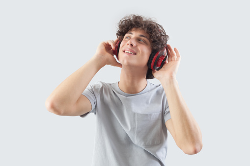 Smiling and handsome, the young man wears headphones and is isolated against a gray background. He looks to the side with his blue eyes while listening to music