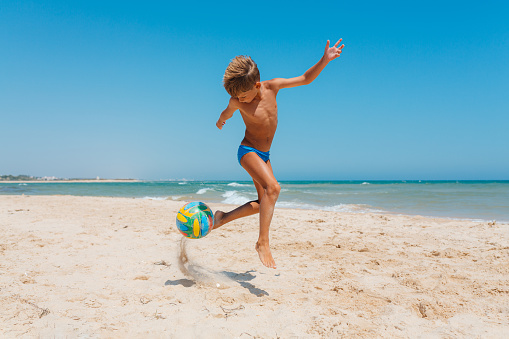 Boy having fun playing and dribbling with walleyball on the beach in the beautiful Algarve Portugal region