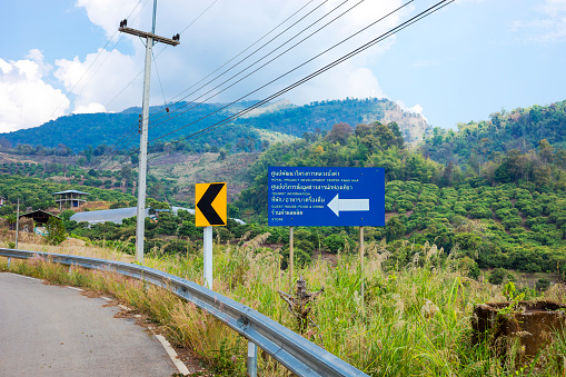 Curved road and road sign and view into mountain landscape around Pang Kha in north Thailand with Royal Development Center and coffee plantations in mountains around Phayao