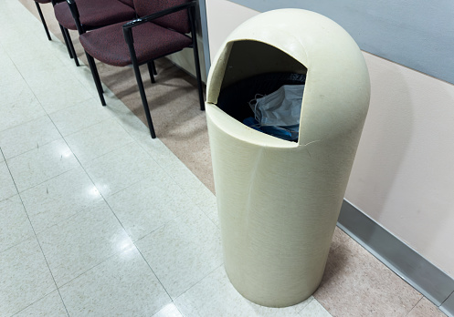 trashcan stands against a white wall, overflowing with crumpled papers, symbolizing waste and clutter