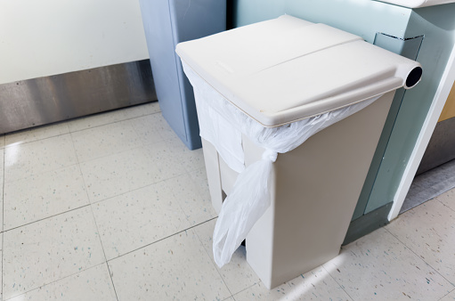 trashcan stands against a white wall, overflowing with crumpled papers, symbolizing waste and clutter