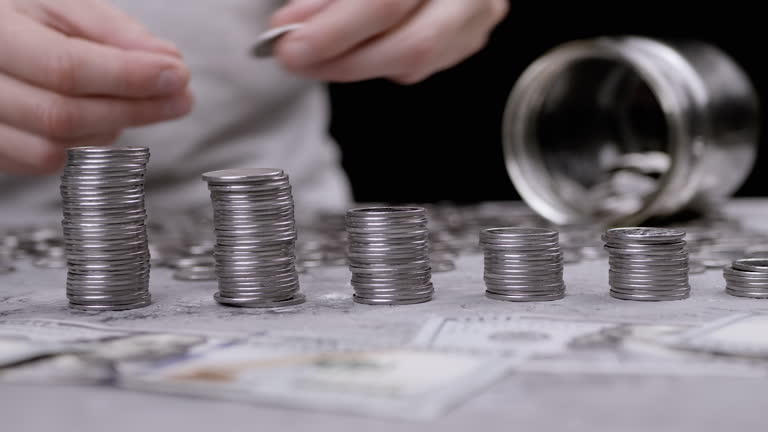 Hands Building a Coin Tower or Stack against the Background of Scattered Money
