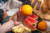 Close-up of hand holding orange against a background of laid out picnic food, selective focus