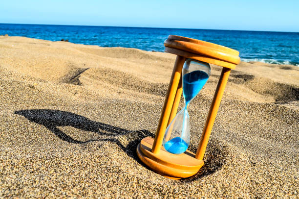 istock A wooden sand timer with blue water in it is on a beach 2149537455