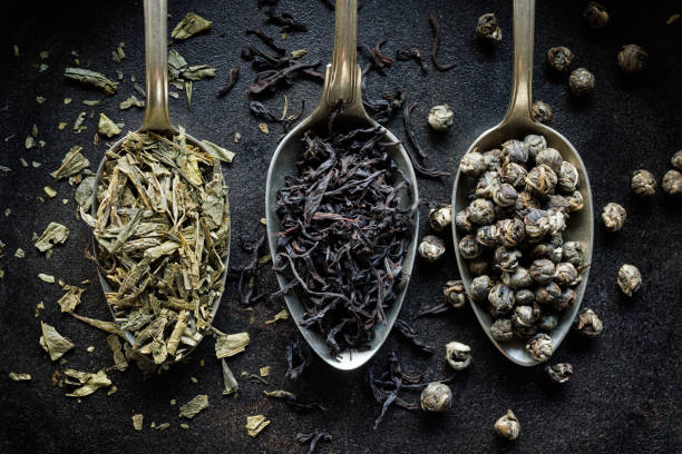 Various types of dried tea on spoons on a black background