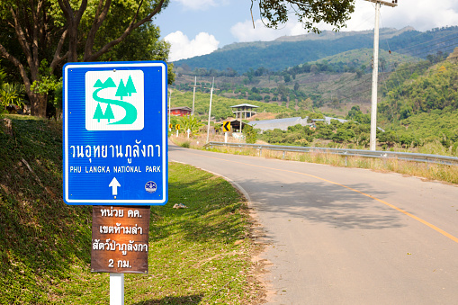 Road sign to Phu Langka National Park in north Thailand seated close to Pang Kha Royal Project And Development Centre coffee shop  in landscape around Pang Kha in north Thailand with Royal Development Center and coffee plantations in mountains around Phayao. Exact location is 9CHV+935, Pha Chang Noi, Pong District, Phayao 56140, Thailand.. At right side is road winding up into mountains