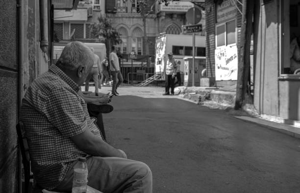 Chios, Greece - July 17, 2017: A narrow alley in the medieval village of Pyrgi (or Pirgi or in Greek: Πυργί) on the Greek Island of Chios in the Aegean Sea. In the background is a man riding a motorcycle. The image was captured on grainy (ISO 400) black and white analogue film by a 35 mm old-fashioned film camera. Pyrgi is part of a group of villages on Chios called the mastic villages (including Mesta, Olympia, Armolia, Vessa, and other villages) because they produced and traded mastic gum from mastic trees. These villages have been added in the List of the Intangible Cultural Heritage of Humanity of UNESCO. The Pyrgi village stands out from the other mastic villages because its houses are decorated with motifs in different traditional shapes. The image is part of a series of black and white analogue photographs of picturesque Greek Island Villages on the Island of Chios.