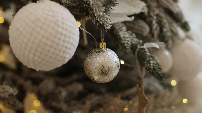 Close up view of beautiful fir branches with shiny white baubles or balls, golden xmas ornaments and lights. Holidays background. Decoration on christmas tree. Festive new 2025 year. Copy space.