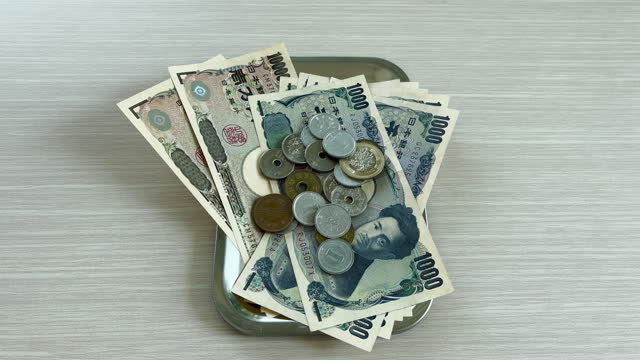 Hands count yen, both banknotes and coins, and place them in a tray for changing for shopping, business or travel.