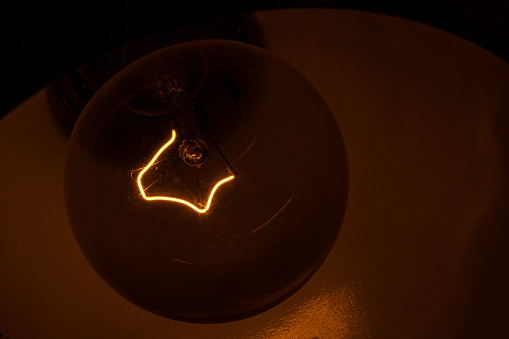 Glowing filament - close-up of incandescent light bulb - dark background with warm light. Taken in Toronto, Canada.