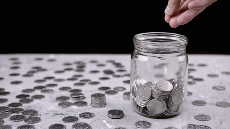 Hands Putting a Handful of Accumulated Silver Coins into a Glass Jar. Close-up