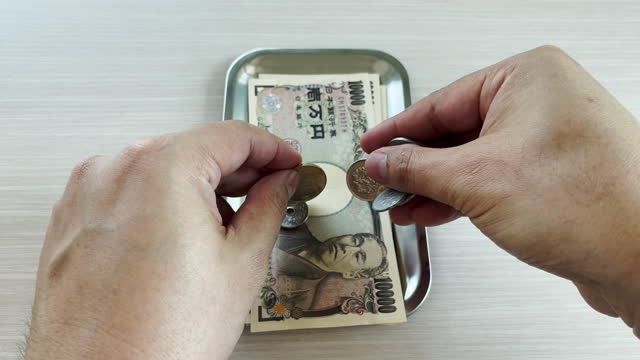 Hands count yen, both banknotes and coins, and place them in a tray for changing for shopping, business or travel.