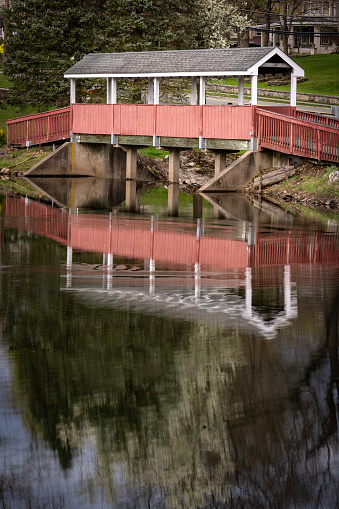 Mahwah, NJ - US- Apr 14, 2024 Vertical view of reflections in the serene Winters Pond in Mahwahs Winters Park, with a beautiful wooden covered bridge.