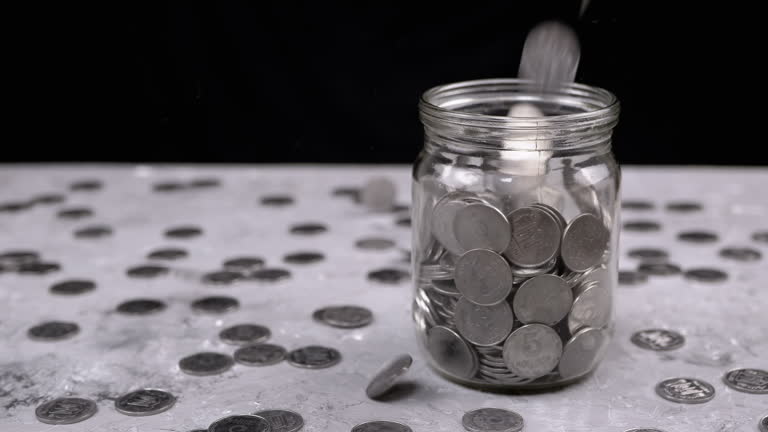 Silver Coins Fall into a Glass Jar against the Background of Scattered Kopecks