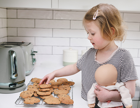 Cute 3 year old girl placing her recently cooked chocolate chip cookies onto a cooling rack