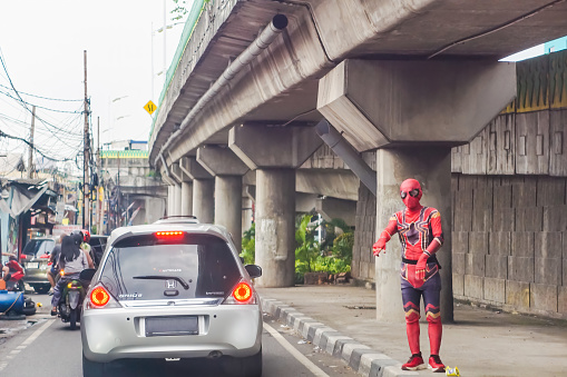 Ciledug, Indonesia - April 14, 2024: An unidentified man wearing a Spider-Man costume stands under an overpass regulating passing vehicles. The spider-man is regulating traffic.