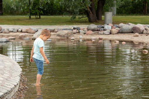A child is wading in the cool water of a city park, he wants to cool his feet on a hot summer day.