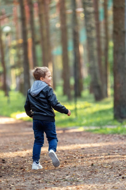 istock A cheerful active little boy in a black leather jacket is running away along the forest path, turned back facing us. 2149548322