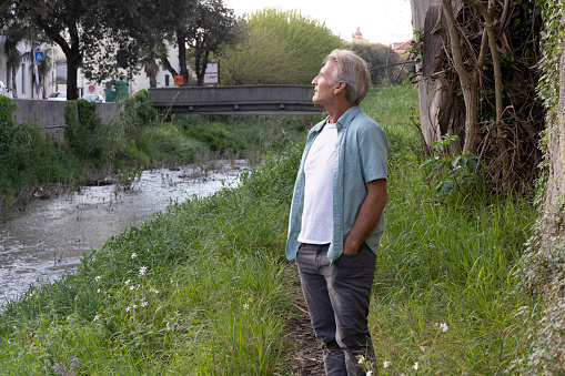 Mature man pauses on riverbank in springtime, Liguria