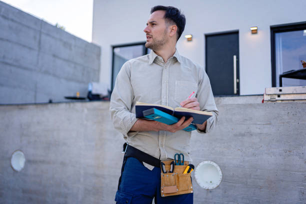 istock Young Caucasian male civil engineer checking blueprints, while standing in front of a renovation project 2149549044