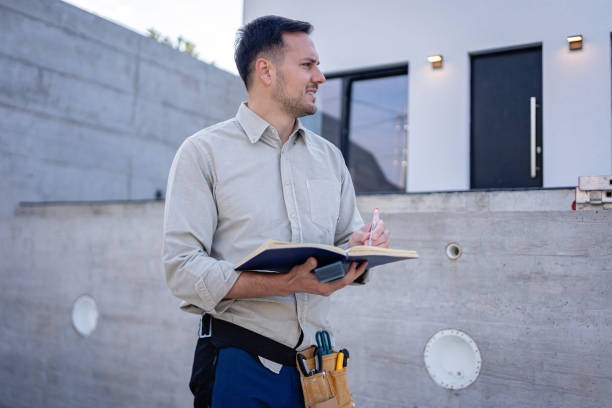 A professional engineer standing in front of a new renovation project Professional engineer standing in front of a modern, newly constructed house, proudly smiling while holding project blueprints Concrete Contractor .
