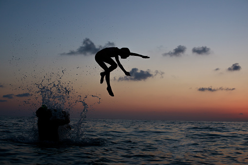 Happy holidays concept. Young kid jumping in the sea under sunset sky with sun and cloud. Happy family on ocean beach