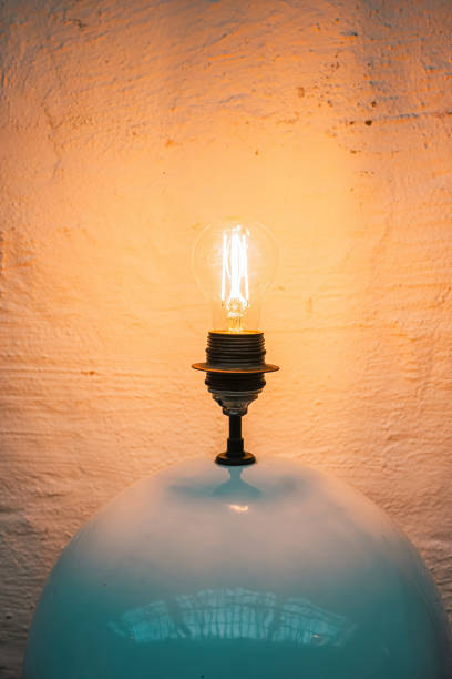 istock Glowing Edison Bulb Over Glass Lampshade Against Textured Wall 2149549639