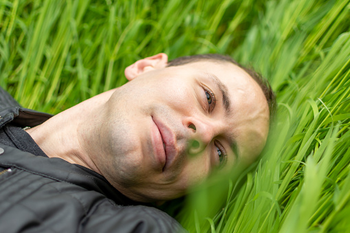 A man blissfully enjoying nature, lying in the grass with his eyes closed, feeling the happiness of being in a grassland meadow